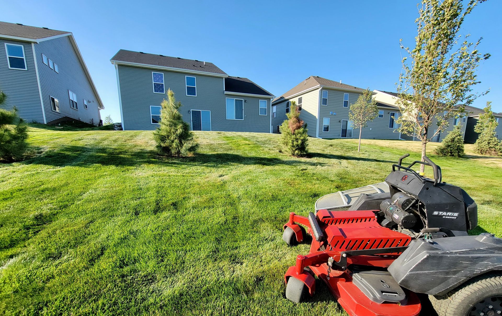 A red lawn mower is sitting in the grass in front of a house.