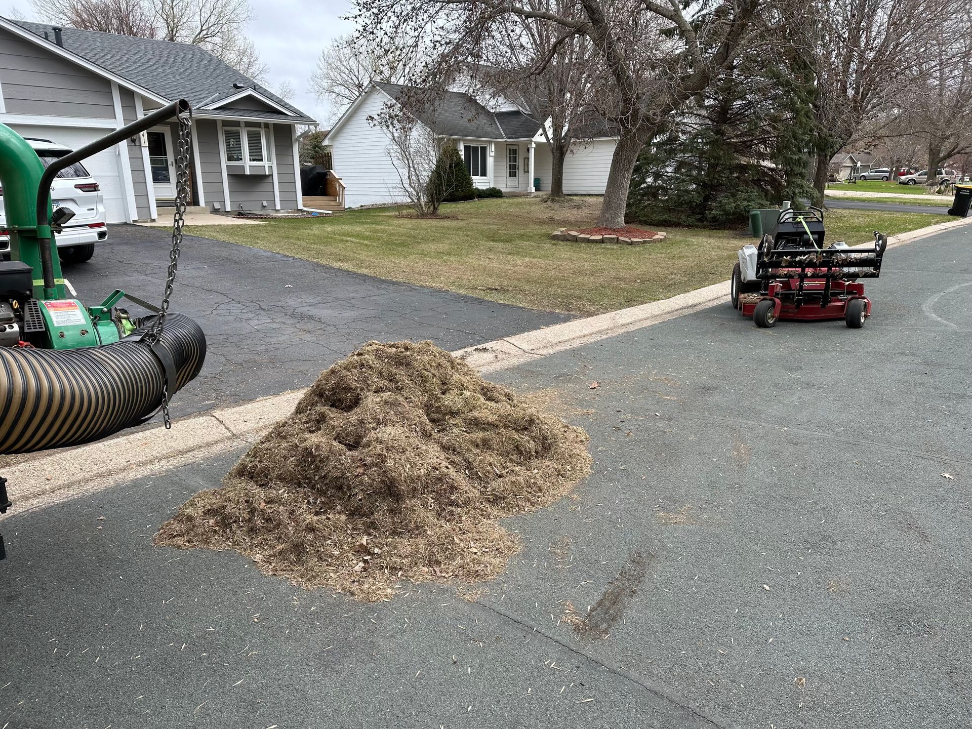 A lawn mower is being used to remove leaves from a driveway.
