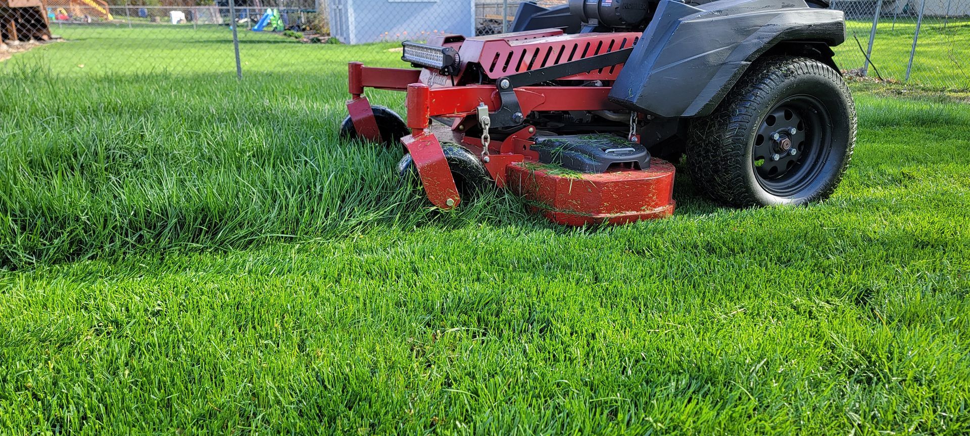 A red lawn mower is cutting a lush green lawn.