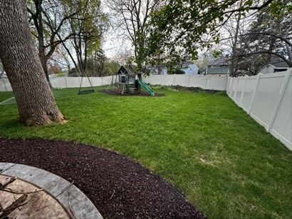 A lush green garden with a brick walkway leading to a stone wall and stairs.