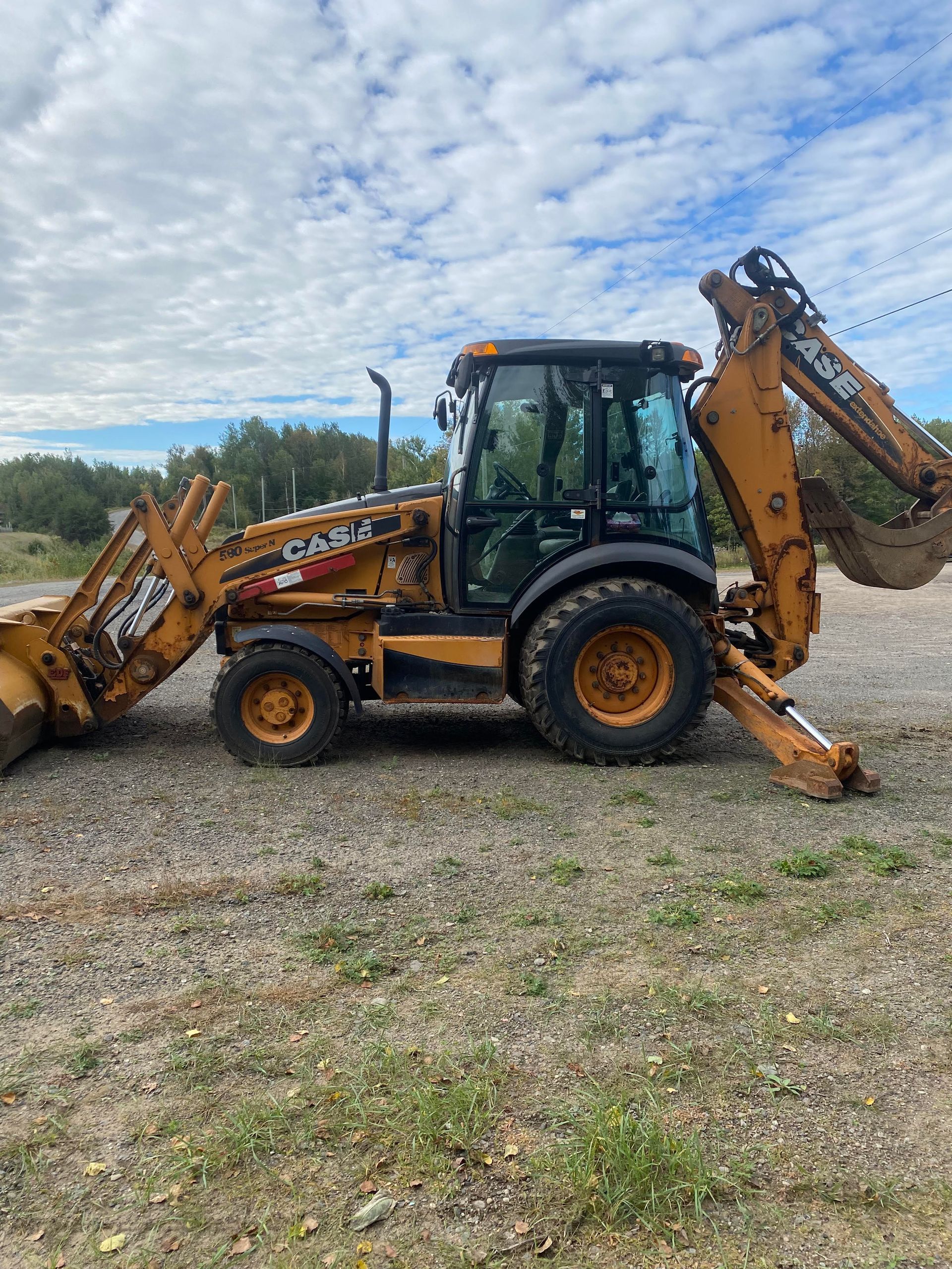 Une rétrocaveuse Case 580 est garée dans un terrain en gravier.