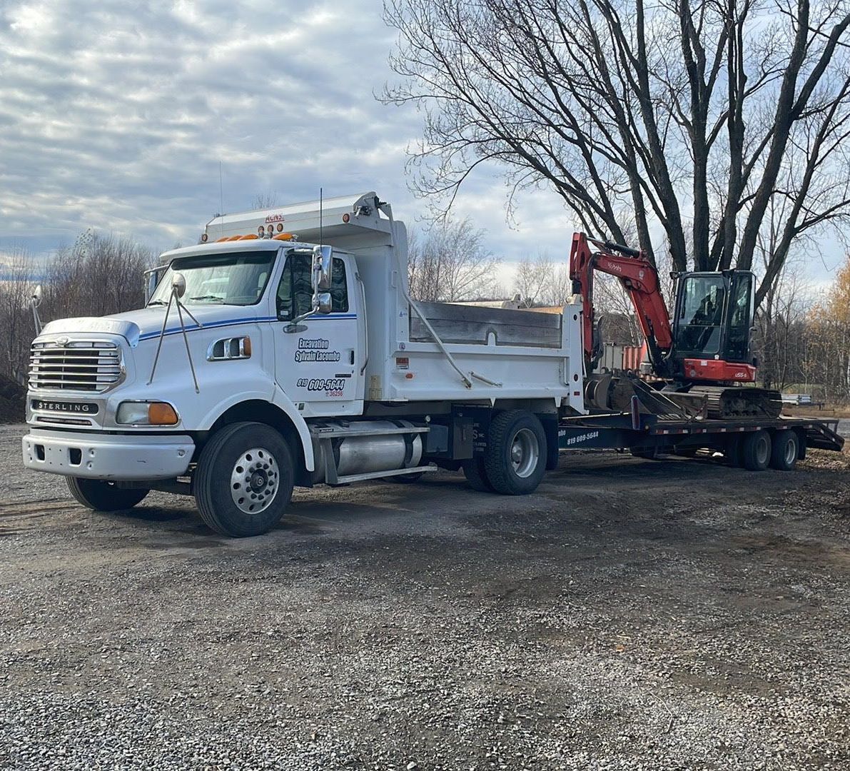 Un camion à benne basculante avec une remorque attachée est garé sur un terrain en gravier.