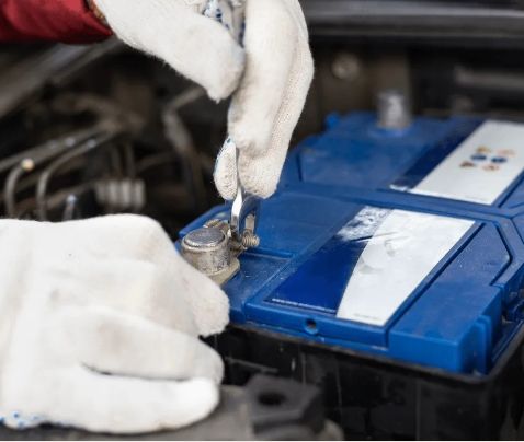 Technician testing a car battery with tools.