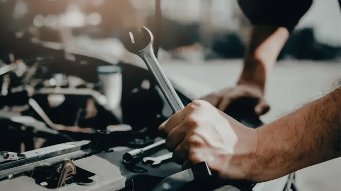 Hands of a mechanic using a wrench on a car part.