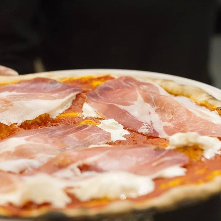 Una persona tiene in mano una pizza con prosciutto e formaggio su un piatto.