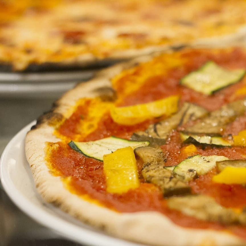 Un primo piano di una pizza con salsa di pomodoro e verdure su un piatto.