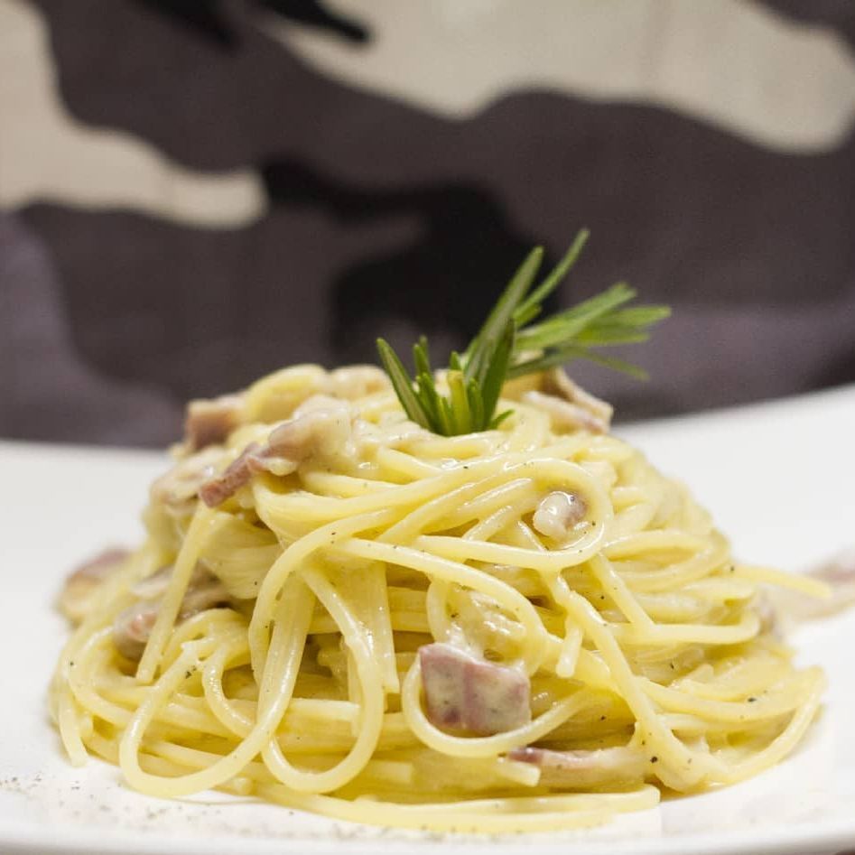 Un primo piano di un piatto di spaghetti con sopra un rametto di rosmarino.