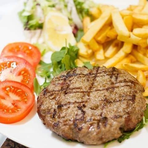 Un piatto bianco sormontato da un hamburger, patatine fritte e pomodori.