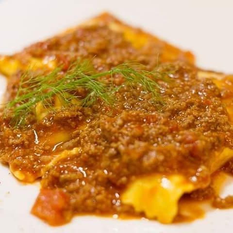 Un primo piano di un pezzo di lasagne con carne e formaggio su un piatto bianco.