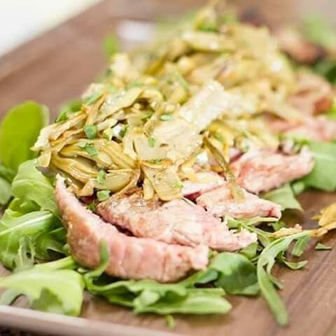 Un primo piano di un piatto di cibo con carne e verdure su un tavolo di legno.