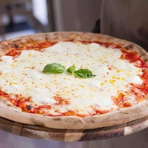 Una pizza è seduta sopra un tagliere di legno.