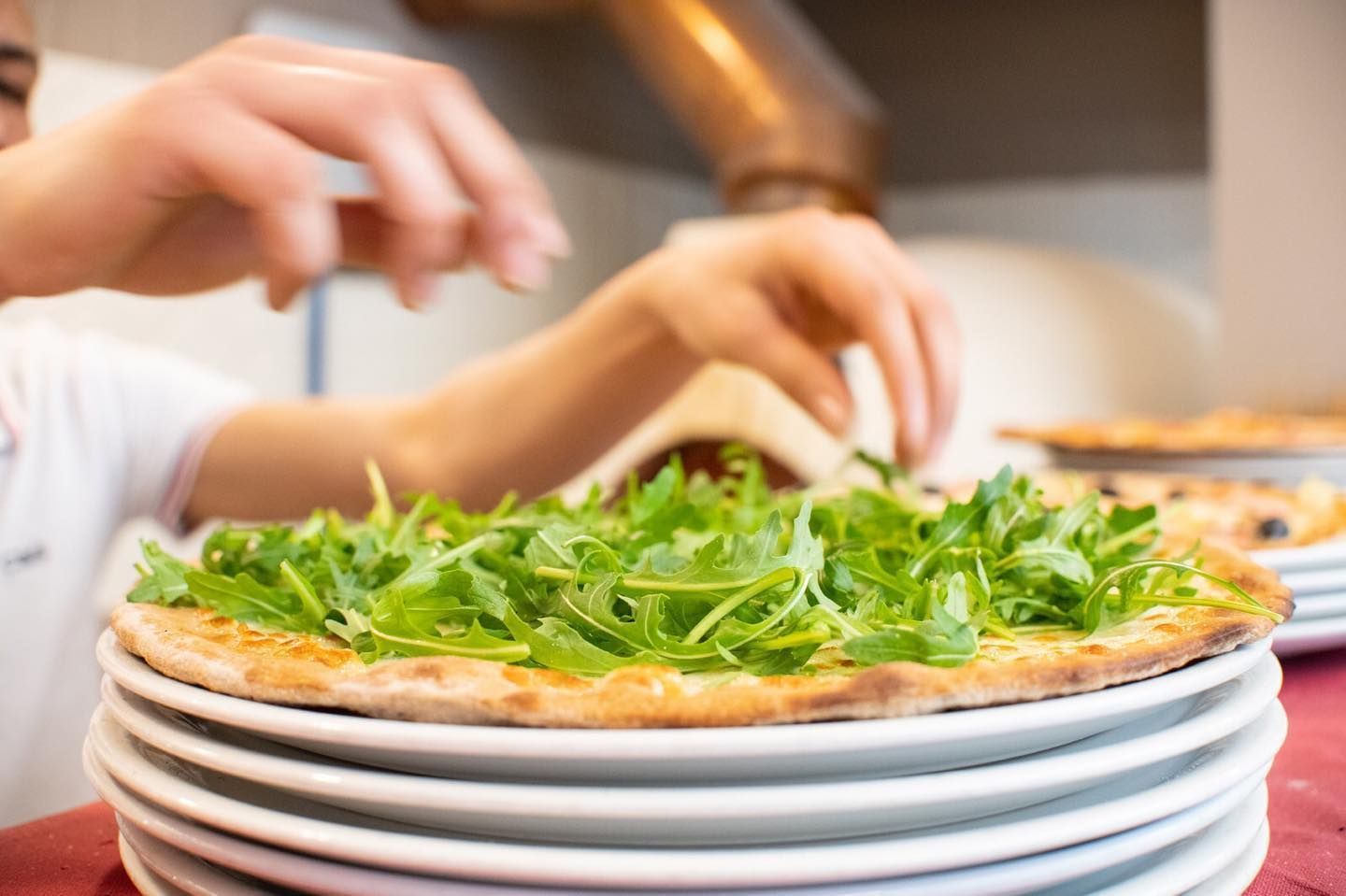 Una persona sta mettendo le verdure sopra una pizza su una pila di piatti.