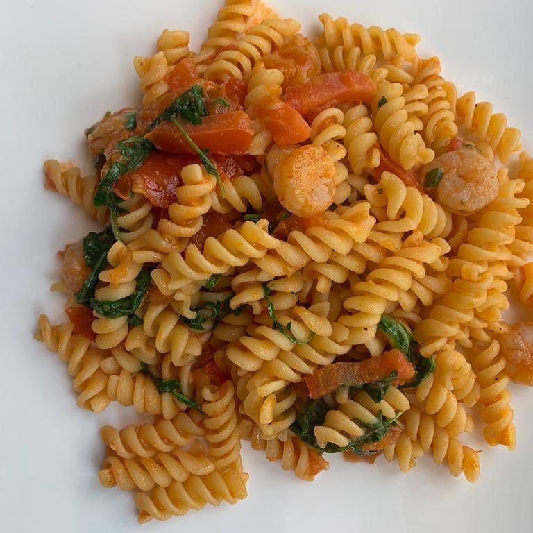 Un primo piano di un piatto di pasta con gamberi e spinaci