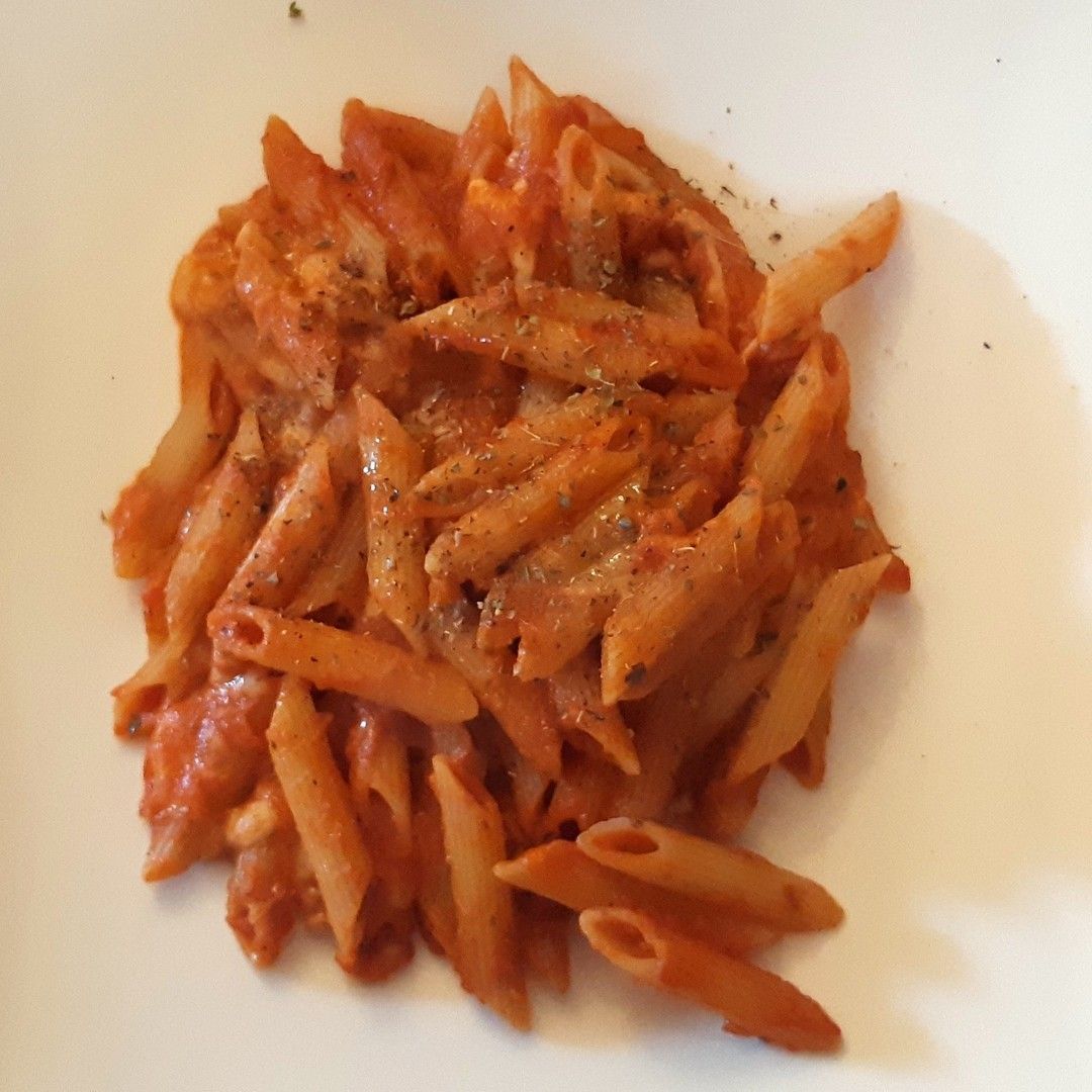 Un piatto bianco condito con pasta e salsa