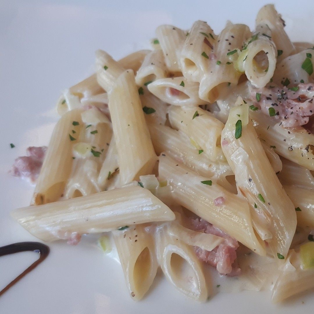 Un piatto bianco condito con penne e salsa