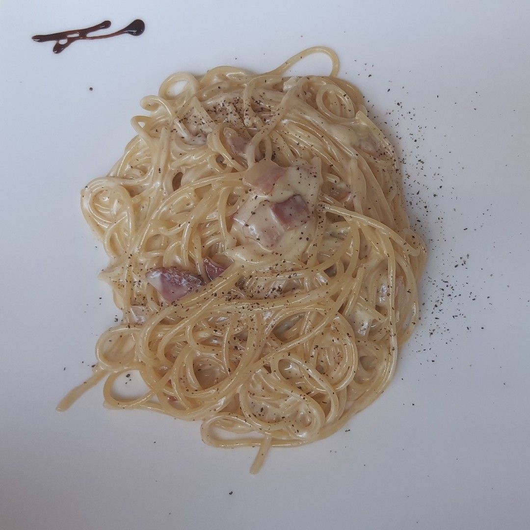 Un piatto bianco condito con spaghetti e salsa
