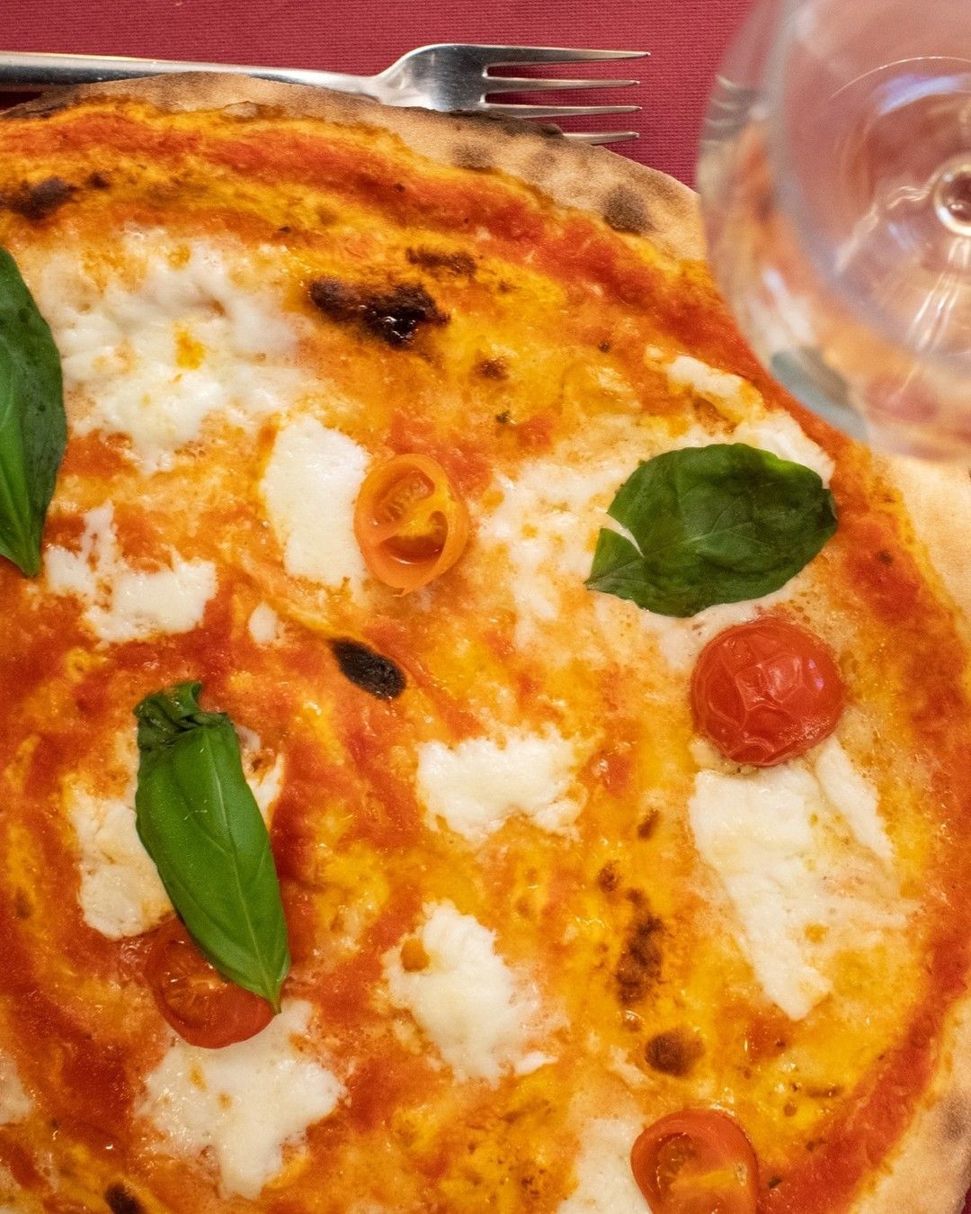 Una pizza con pomodoro, formaggio, basilico e un bicchiere d'acqua su un tavolo.