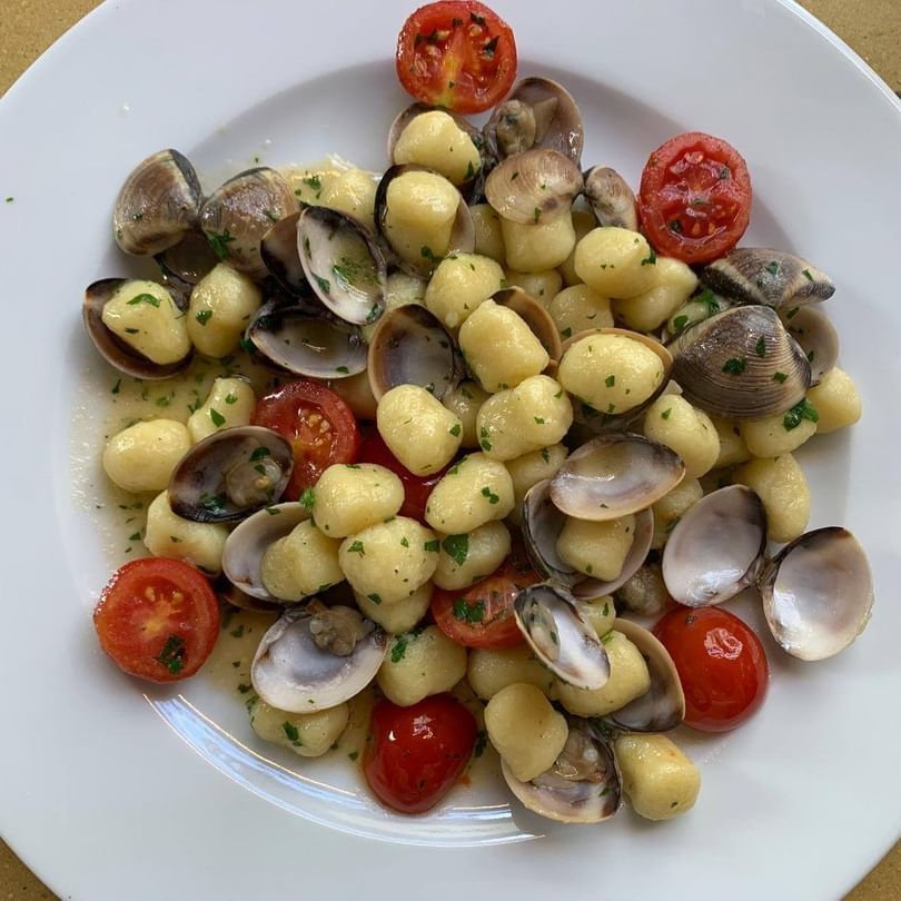Un piatto bianco condito con gnocchi vongole e pomodorini