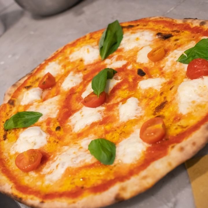Su un tavolo è seduta una pizza con pomodoro e basilico.