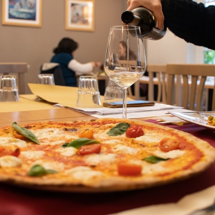 Una persona che versa il vino in un bicchiere accanto a una pizza
