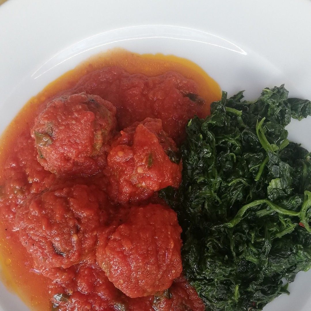 Un piatto bianco condito con polpette e spinaci in salsa di pomodoro.