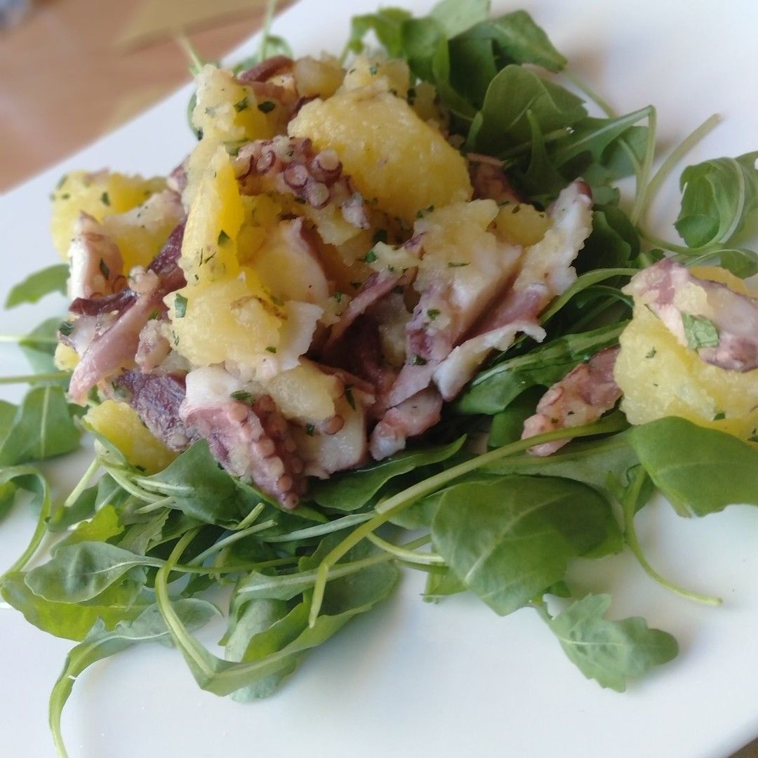 Un piatto bianco condito con un'insalata di patate e polpo