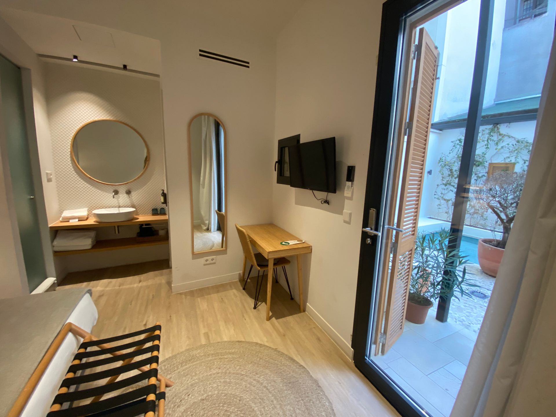 A room with a desk , television , mirror and sliding glass door.