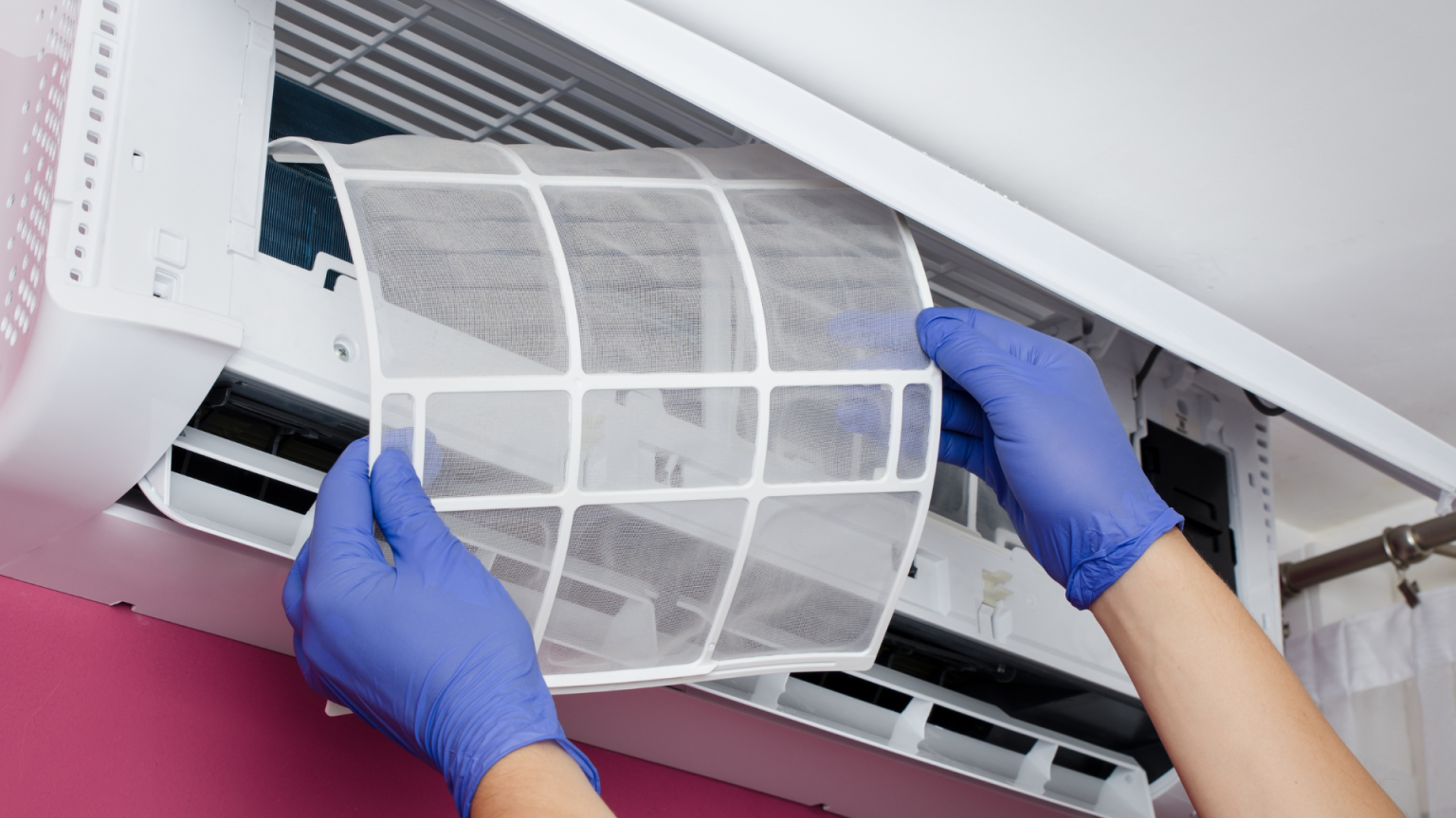 A person wearing blue gloves is cleaning an air conditioner.