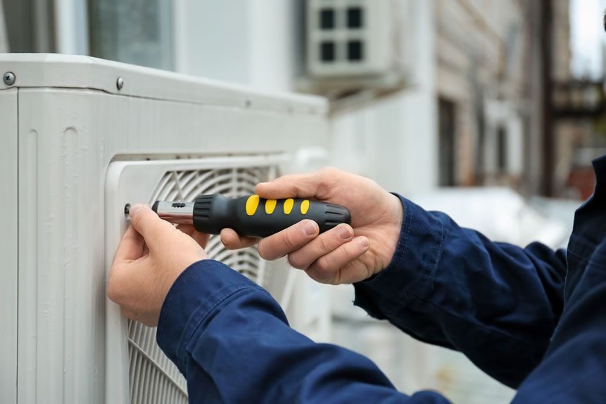 A man is fixing an air conditioner with a screwdriver.