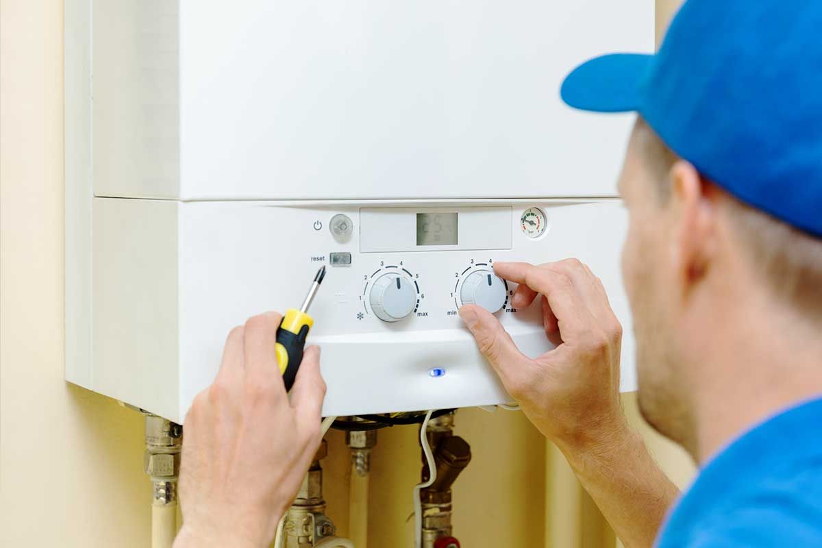 A man is fixing a boiler with a screwdriver.