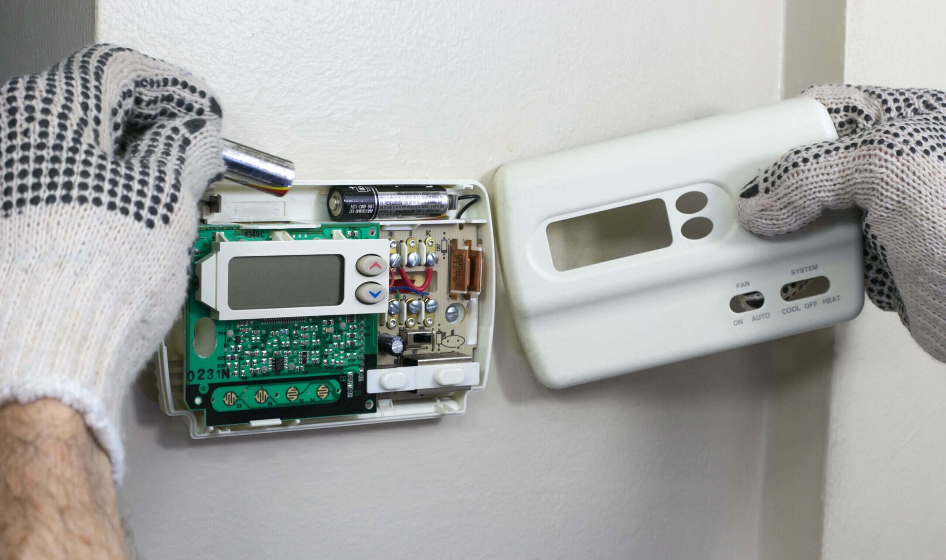 A person wearing gloves is fixing a thermostat on a wall.