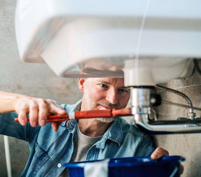 A man is fixing a sink with a wrench.