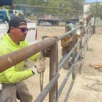 Person in yellow shirt working on metal fence outdoors.