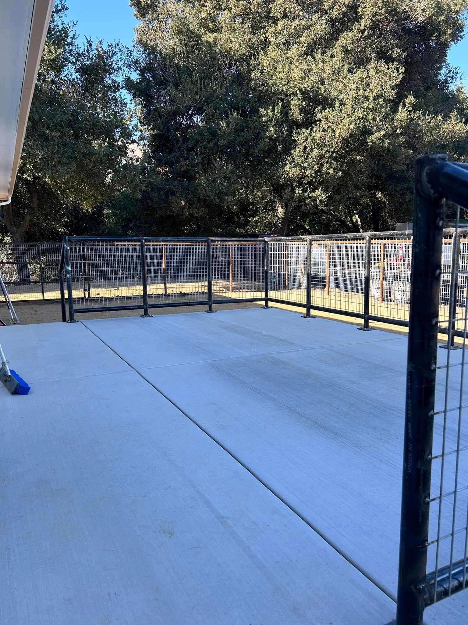 Outdoor concrete patio with metal railings and bike racks, with trees in the background.