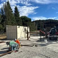 Two people working near a large container in a rural outdoor setting.