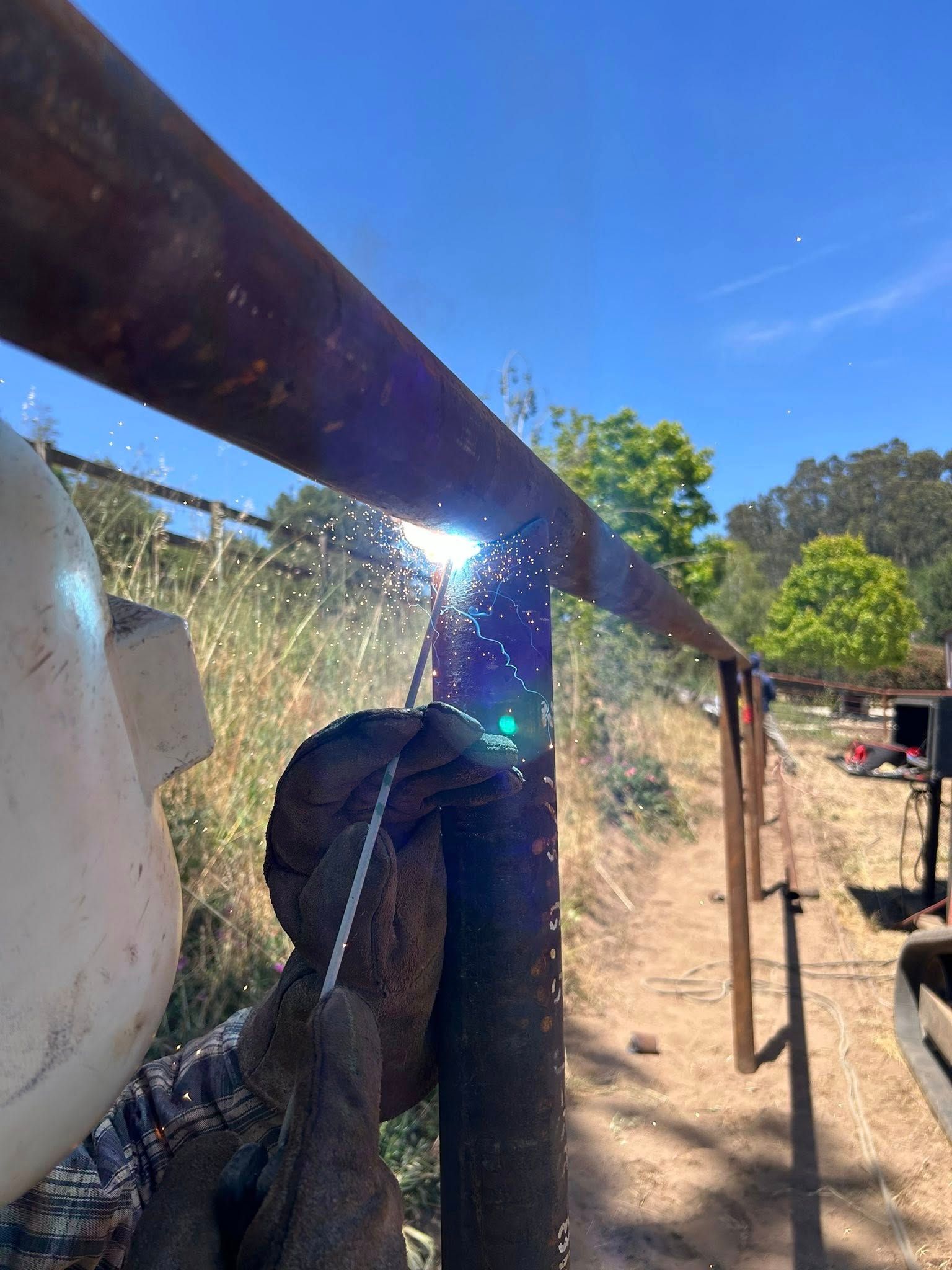 Welder welding metal fence on a sunny day. Sparks fly.