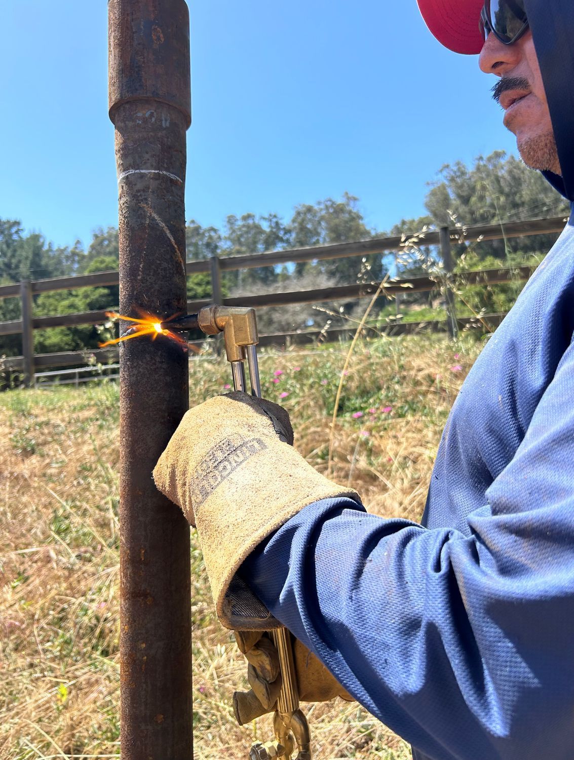 Man welding a metal post outdoors, sparks flying.