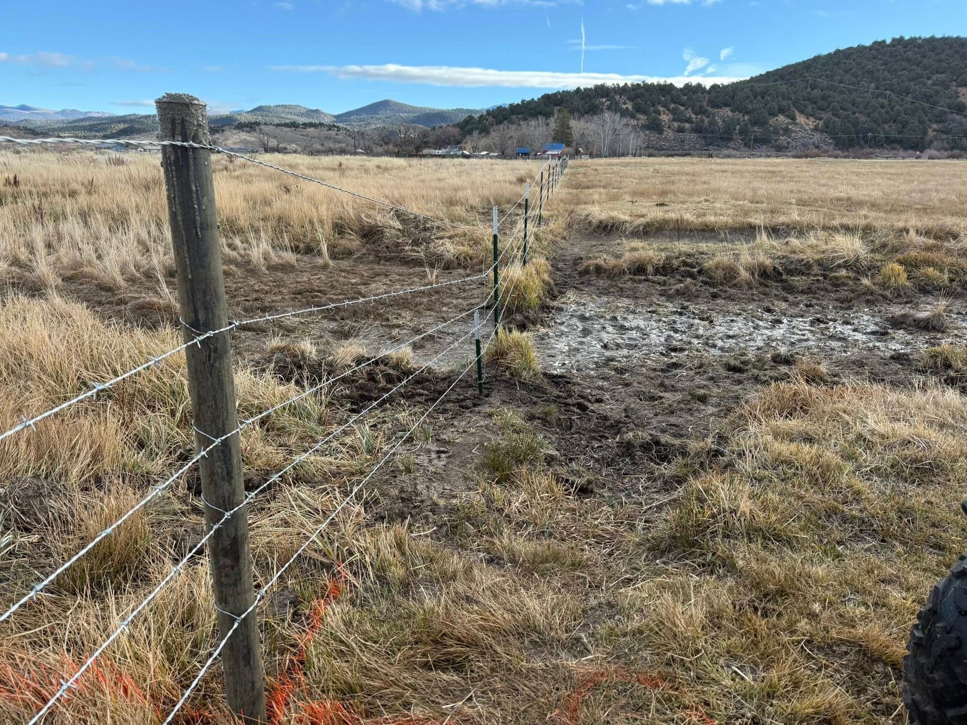 Barbed wire fence in a field of dry grass, mountains in the distance under a blue sky.