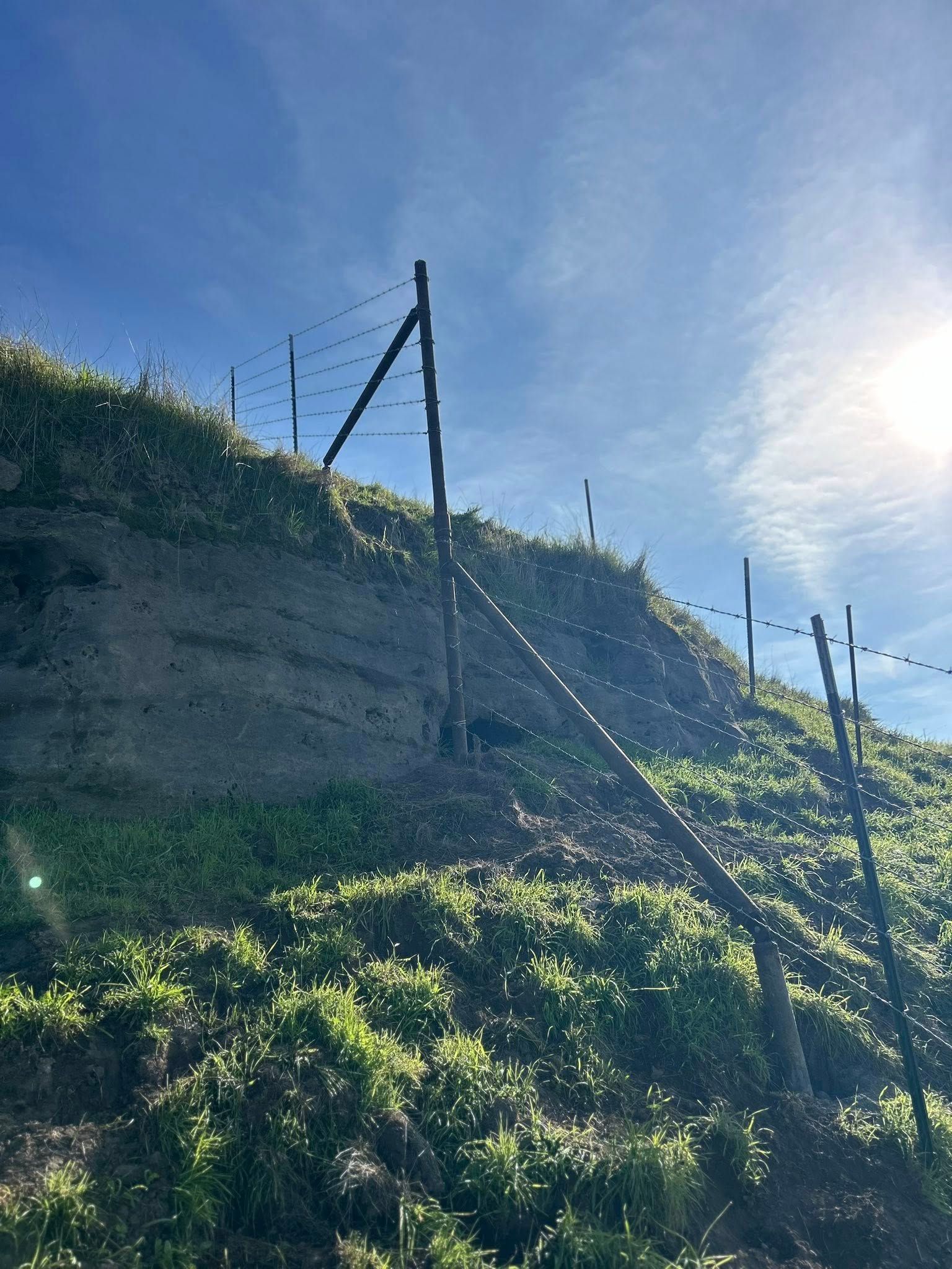 A hillside with a wooden fence stretching upwards towards a bright blue sky.