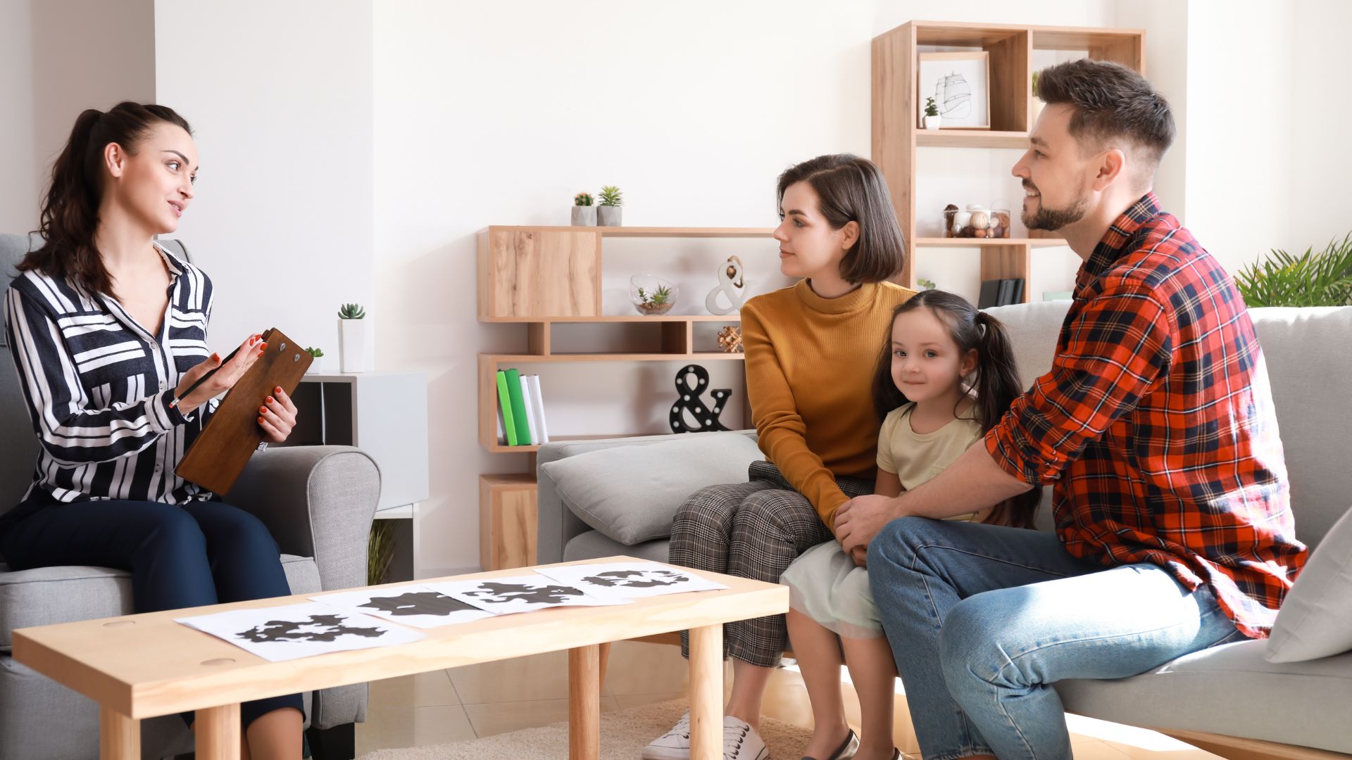 A therapist talking with a family of three in a living room; the family is seated on a sofa.