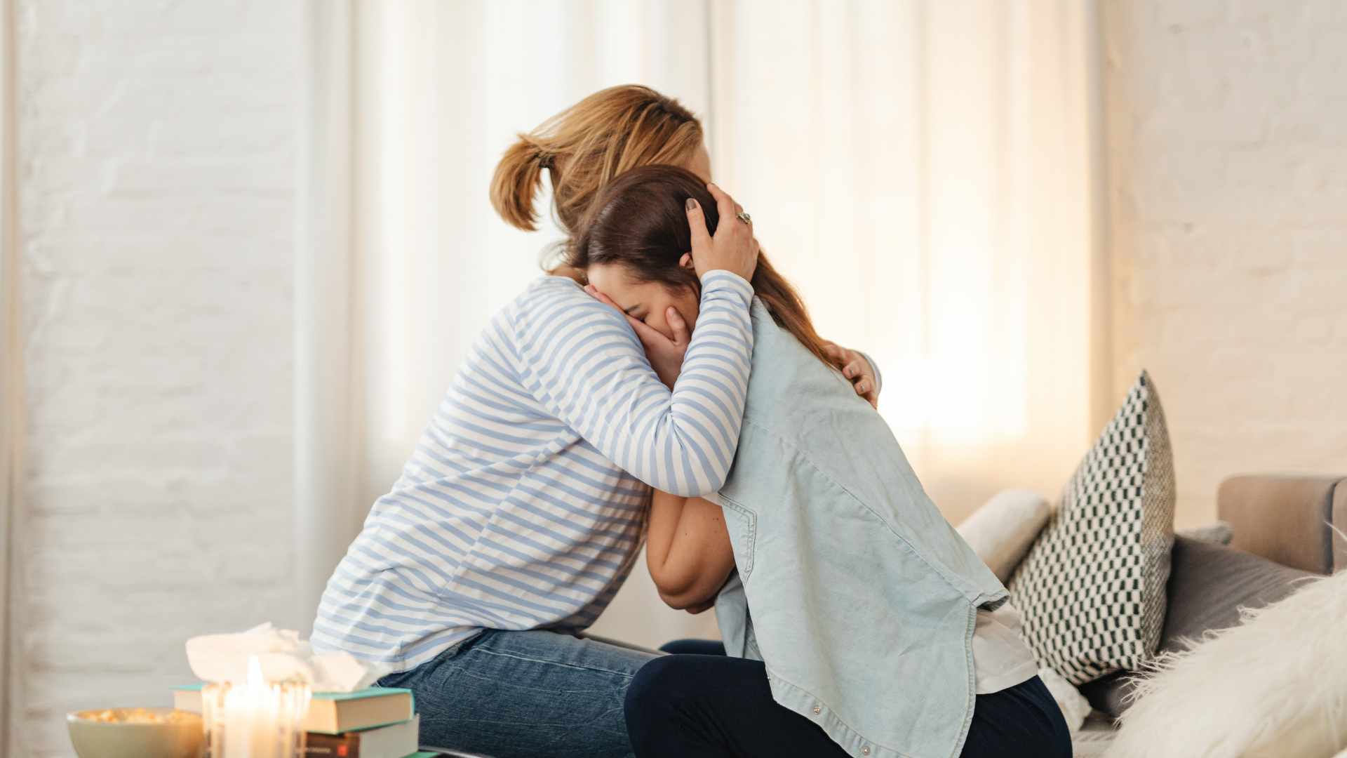 Woman embracing a weeping person indoors, offering comfort.