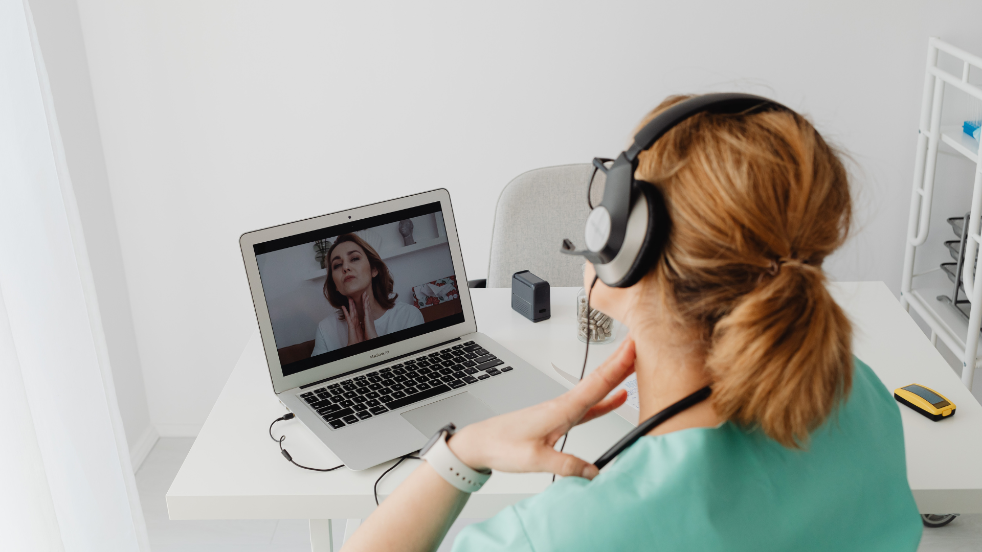 Woman in scrubs with headset on, using laptop for a telehealth consultation.