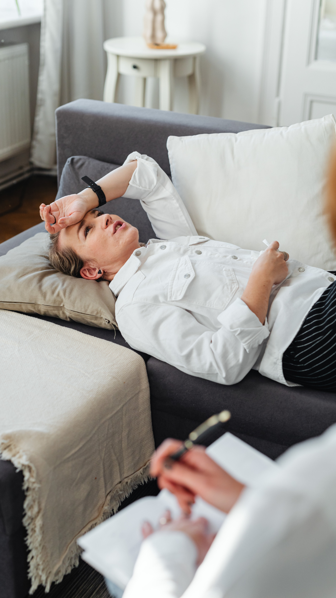 Person lying on a sofa, hand on forehead, in a therapy session.