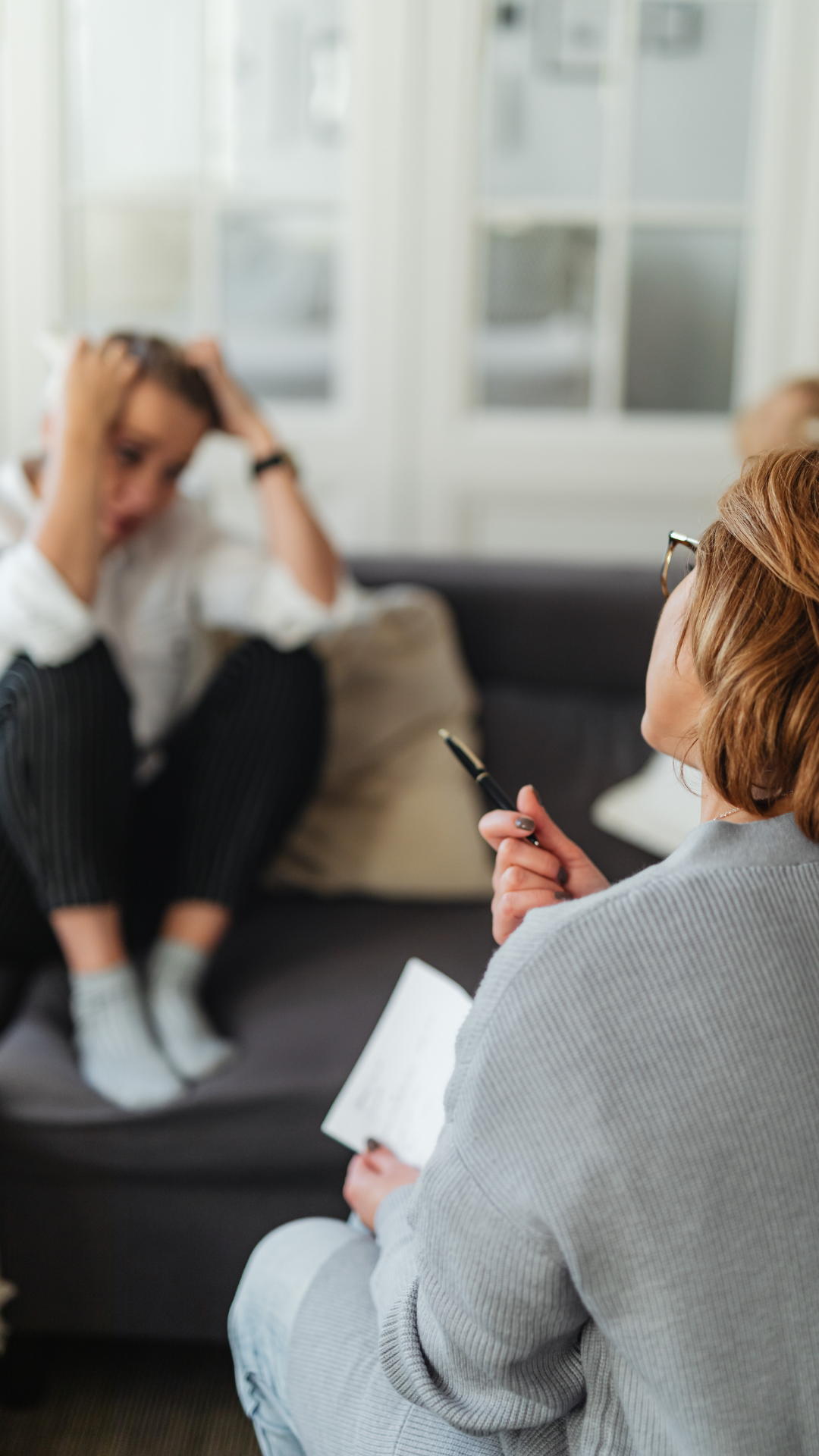 Person on couch with head in hands; therapist with pen and notepad.