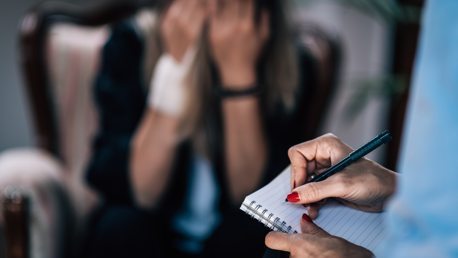 Therapist taking notes during a session; patient with head in hands in an armchair.