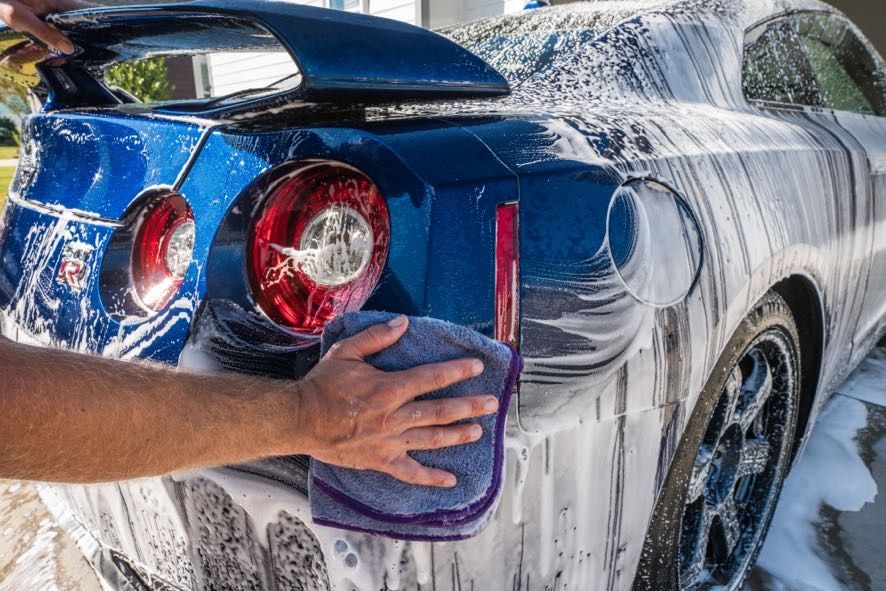 A person is washing a blue sports car with foam and a towel.