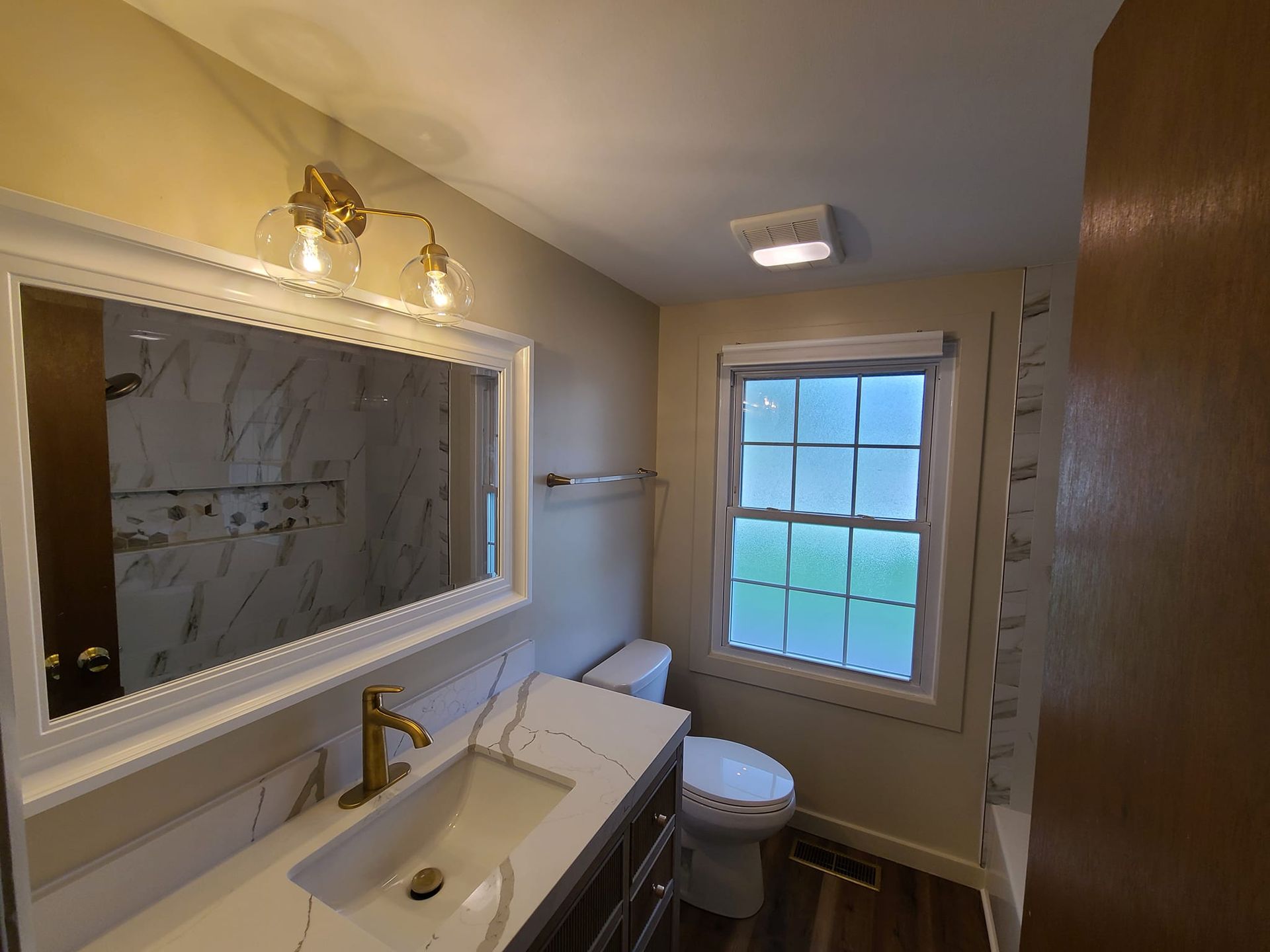 A bathroom with a toilet , sink , mirror and window.