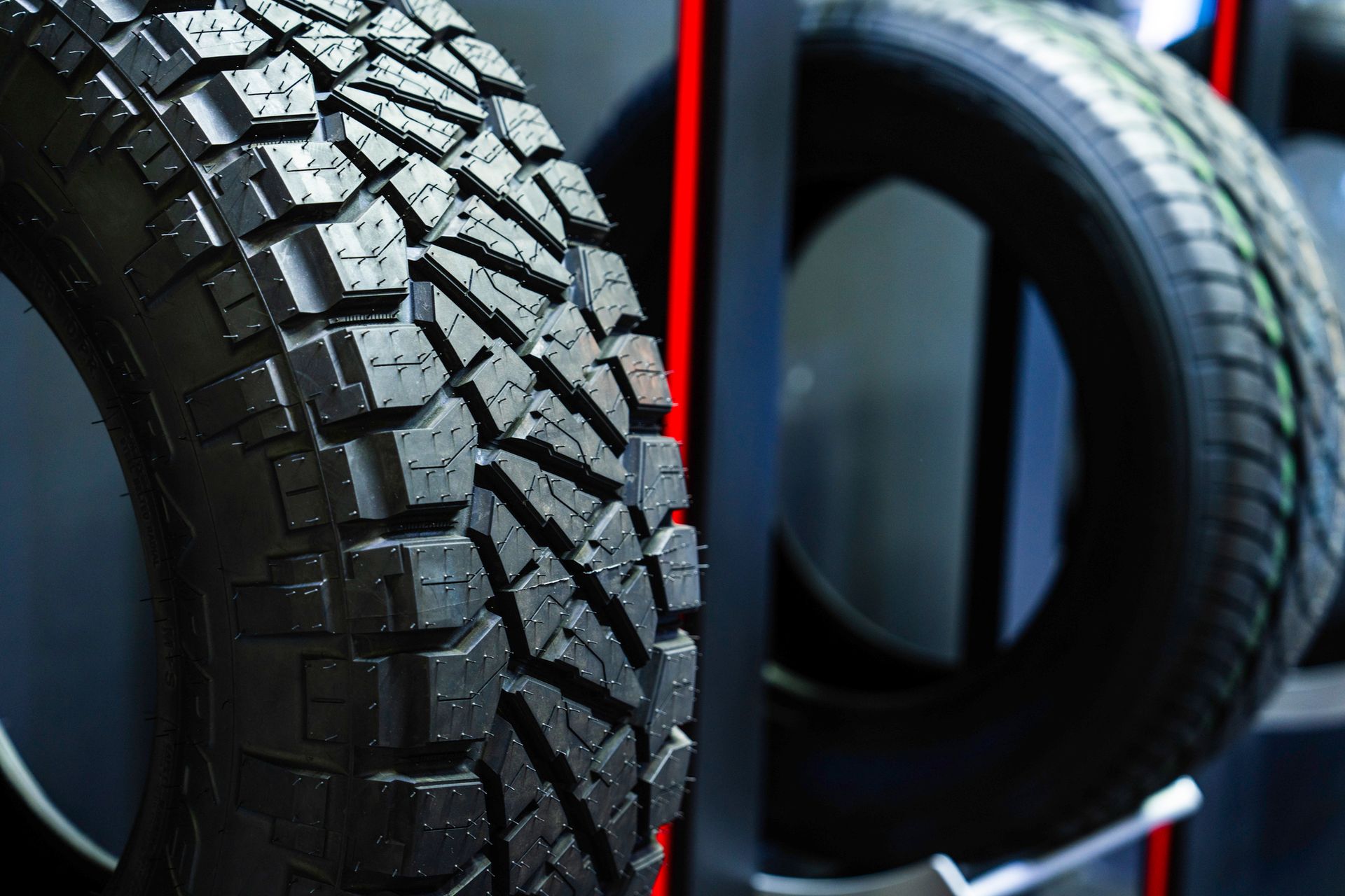Close-up of black tire tread; another tire in background, setting is an auto shop.