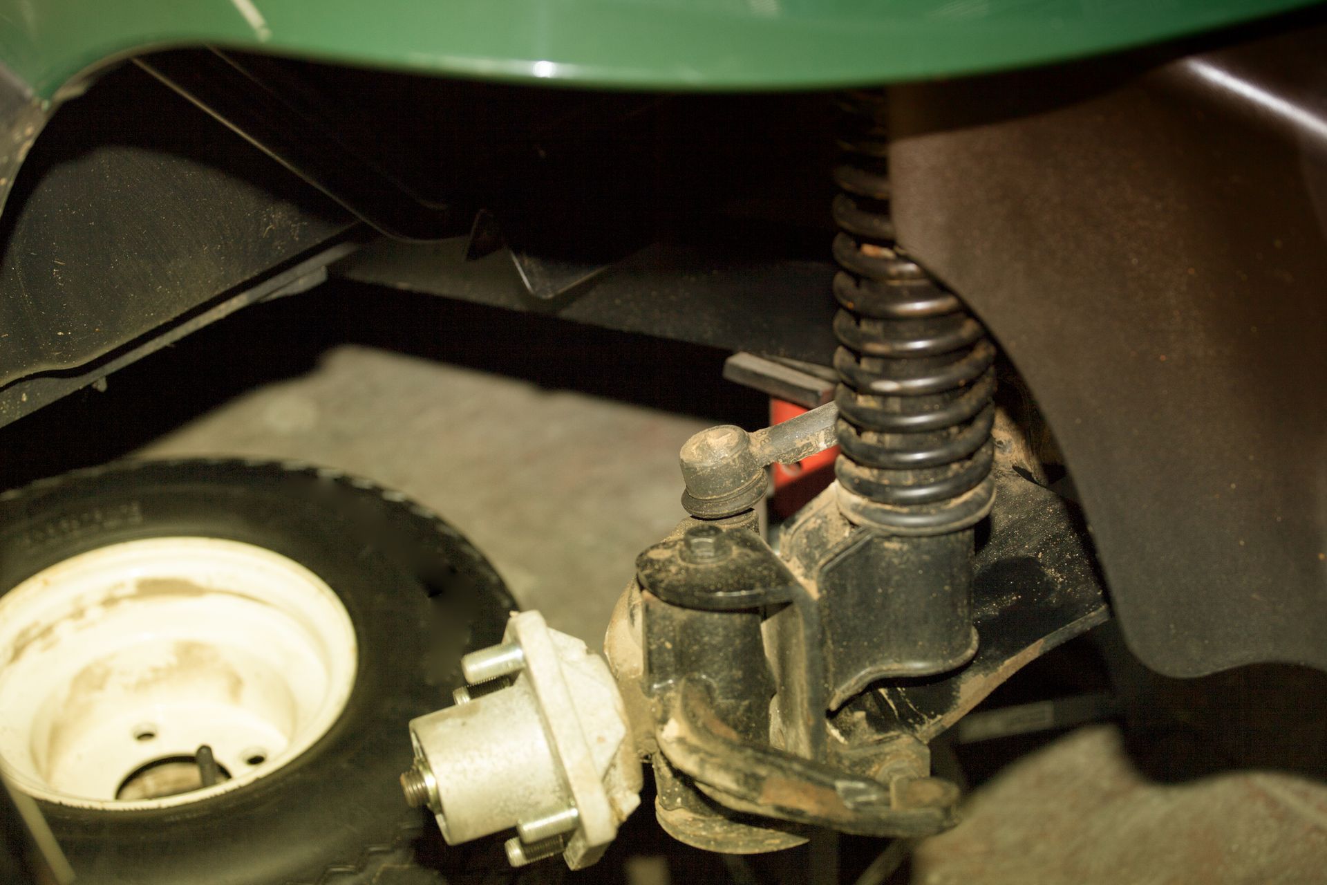 Green golf cart front suspension, showing a tire, shock absorber, and steering components.