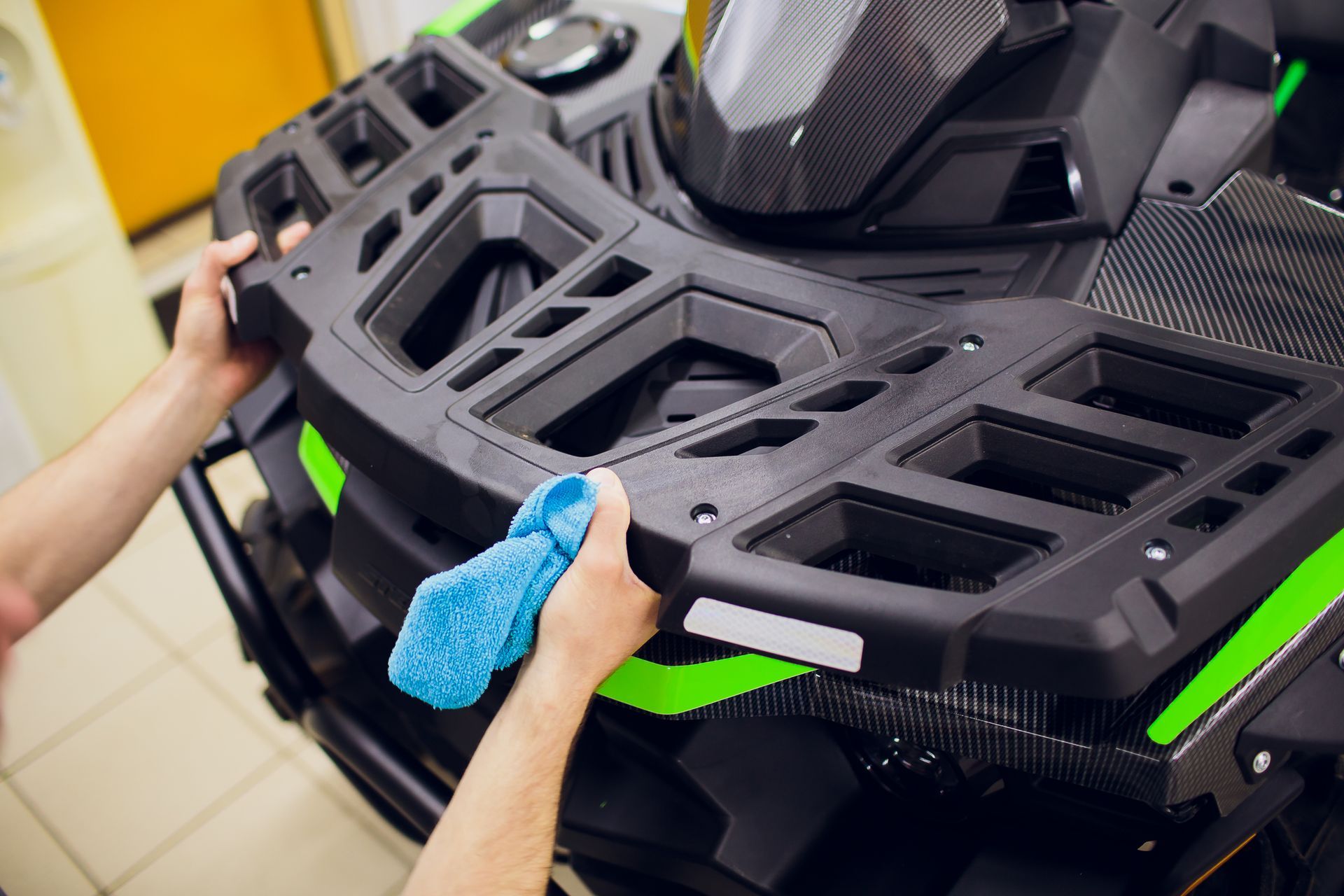 Hands cleaning a black and green ATV rack with a blue cloth.
